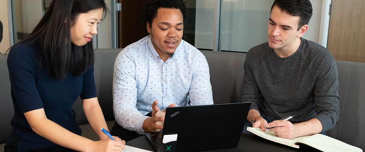 Graduate students looking at a computer and taking notes